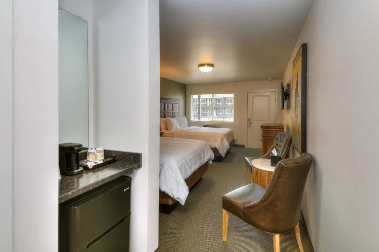 A hotel room with two beds, a desk area, and a mini-fridge.