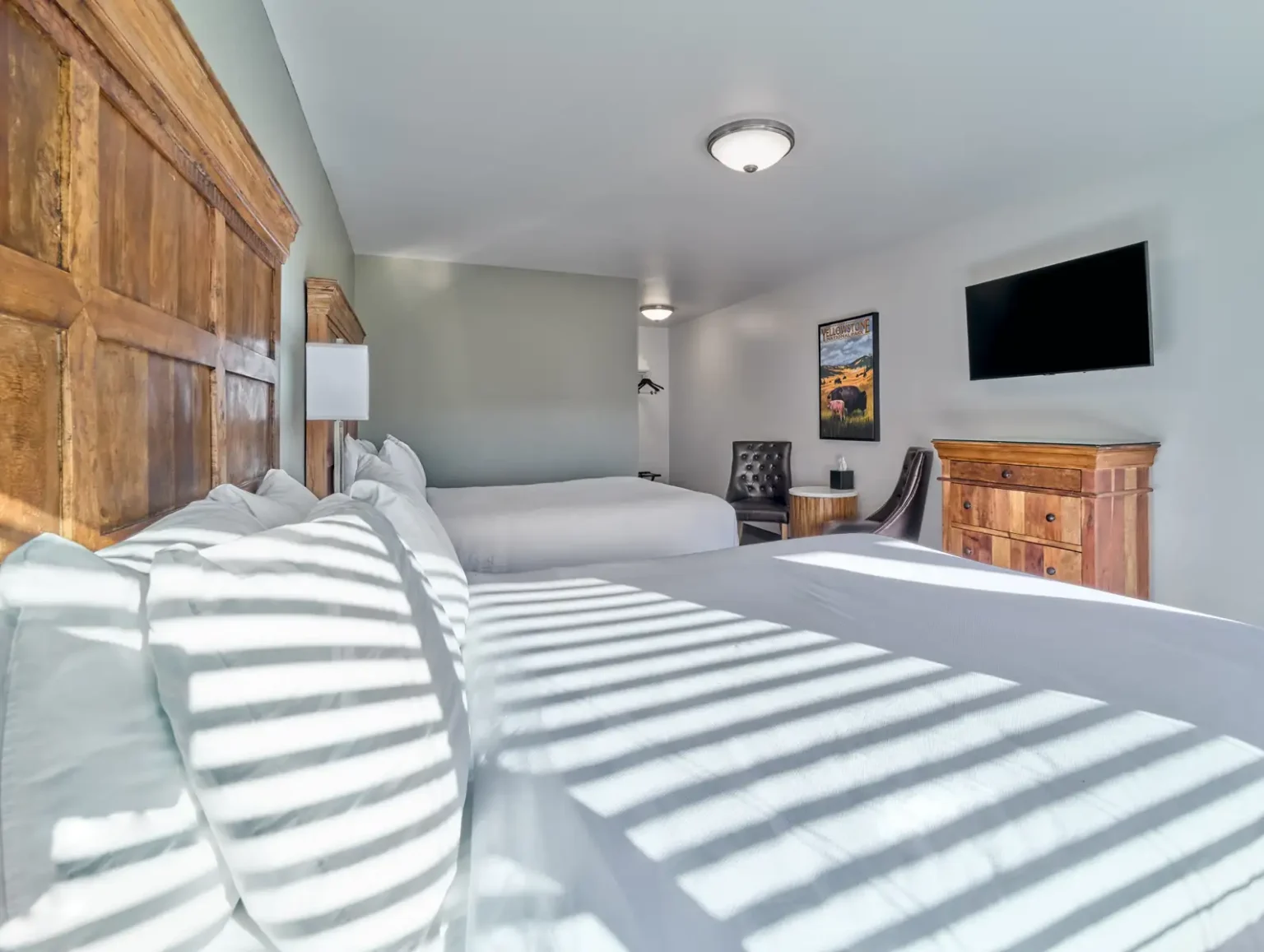 A hotel room with two beds, a wooden dresser, and a flat screen TV on the wall.
